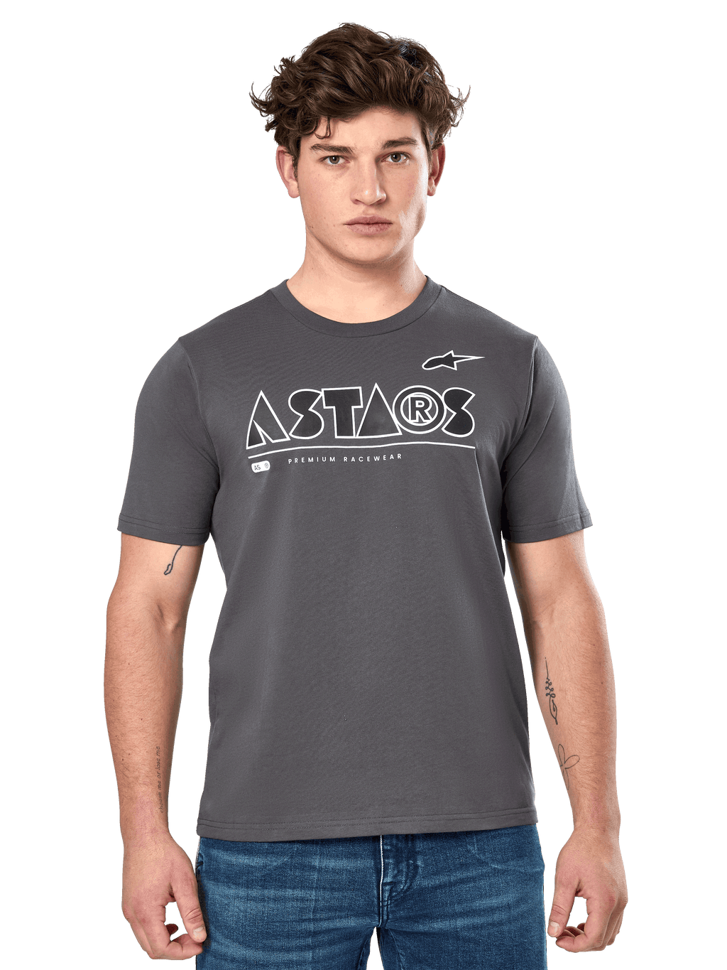 Alpinestars Cereal CSF Tee, antracietgrijs T-shirt met korte mouwen, gedragen door een mannelijk model met een blauwe jeans, wit geometrisch ASTARS-logo en 'Premium Racewear'-tekst, casual motorsport-geïnspireerde lifestyle kleding
