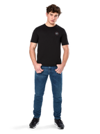 Alpinestars Dot Carbon CSF Tee, T-shirt met korte mouwen, zwart, klein rond Astars Dot-logo op de borst, gedragen met blauwe jeans en zwarte sneakers, casual motorsport streetwear
