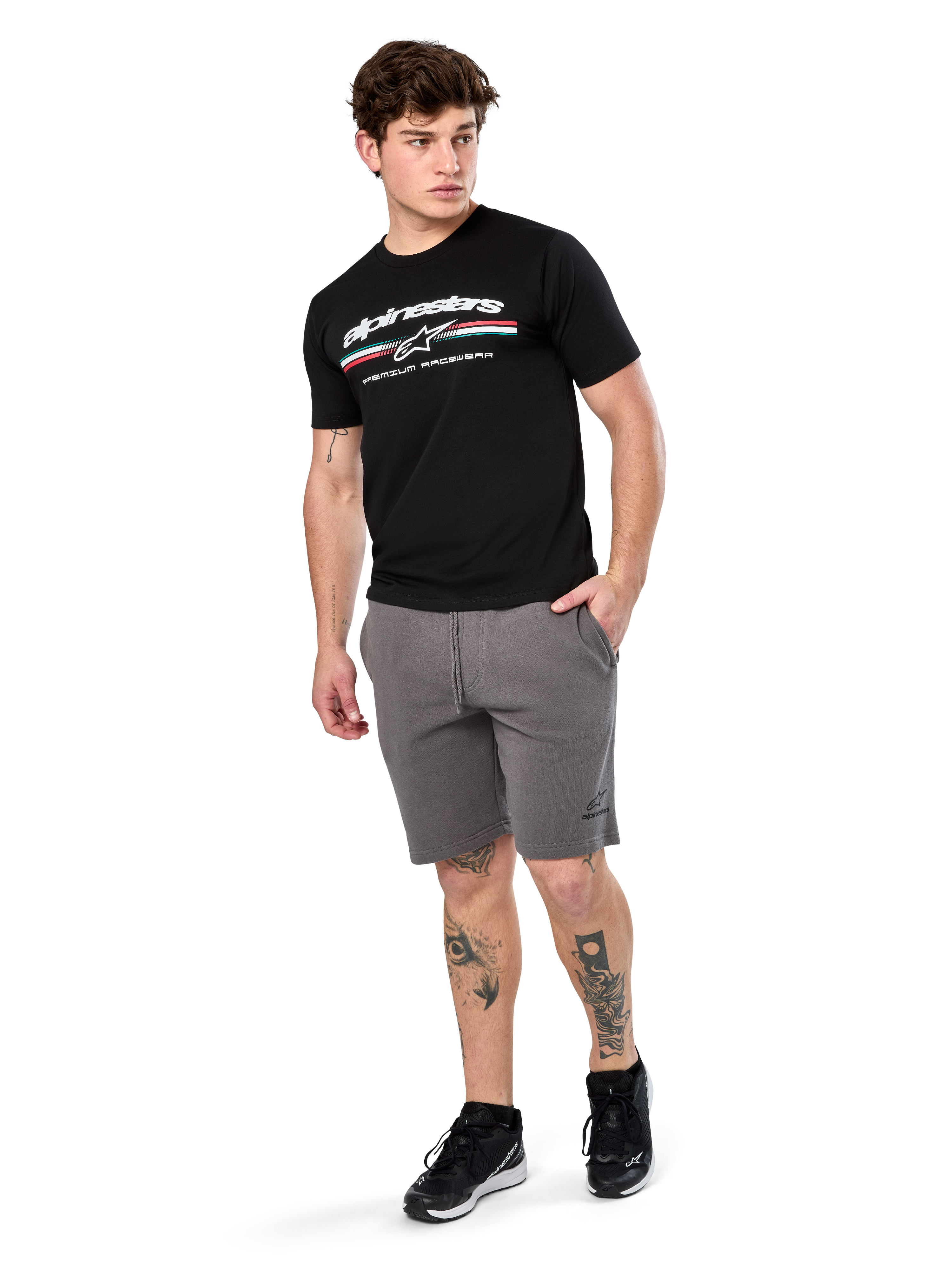 Alpinestars Prevail Csf Tee, T-shirt met korte mouwen, zwart, wit Alpinestars-logo met driekleurige paddock-streep, gedragen met grijze shorts en zwarte sneakers, casual motorsport streetwear
