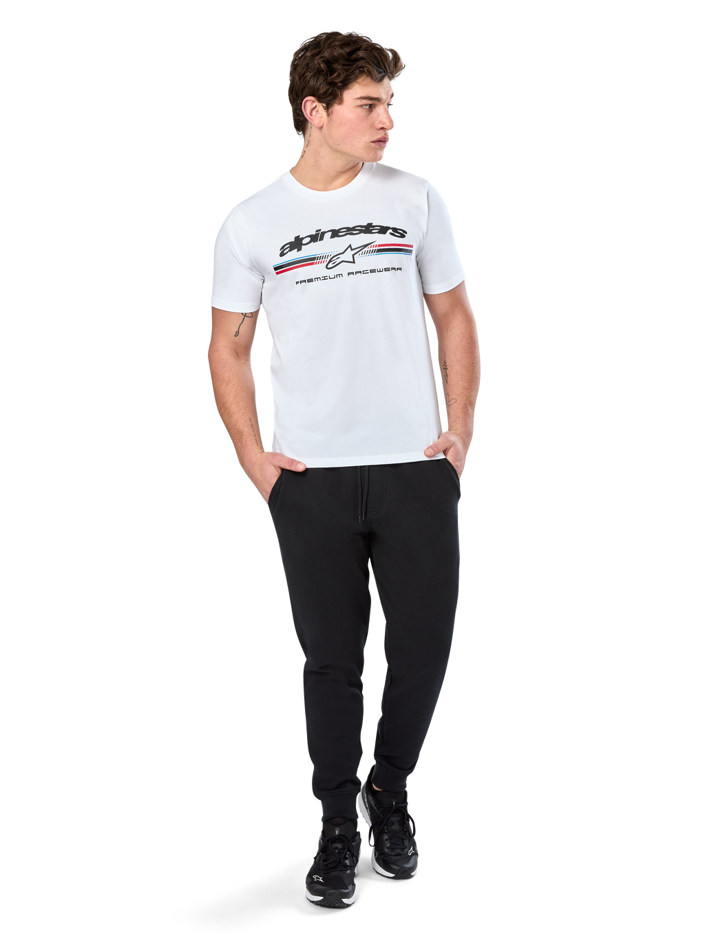 Alpinestars Prevail CSF Tee, T-shirt met korte mouwen, wit, met een driekleurig logo in paddock-stijl op de borst en Alpinestars-branding, gedragen door een model met een zwarte joggingbroek en zwarte sneakers, casual motorsport streetwear