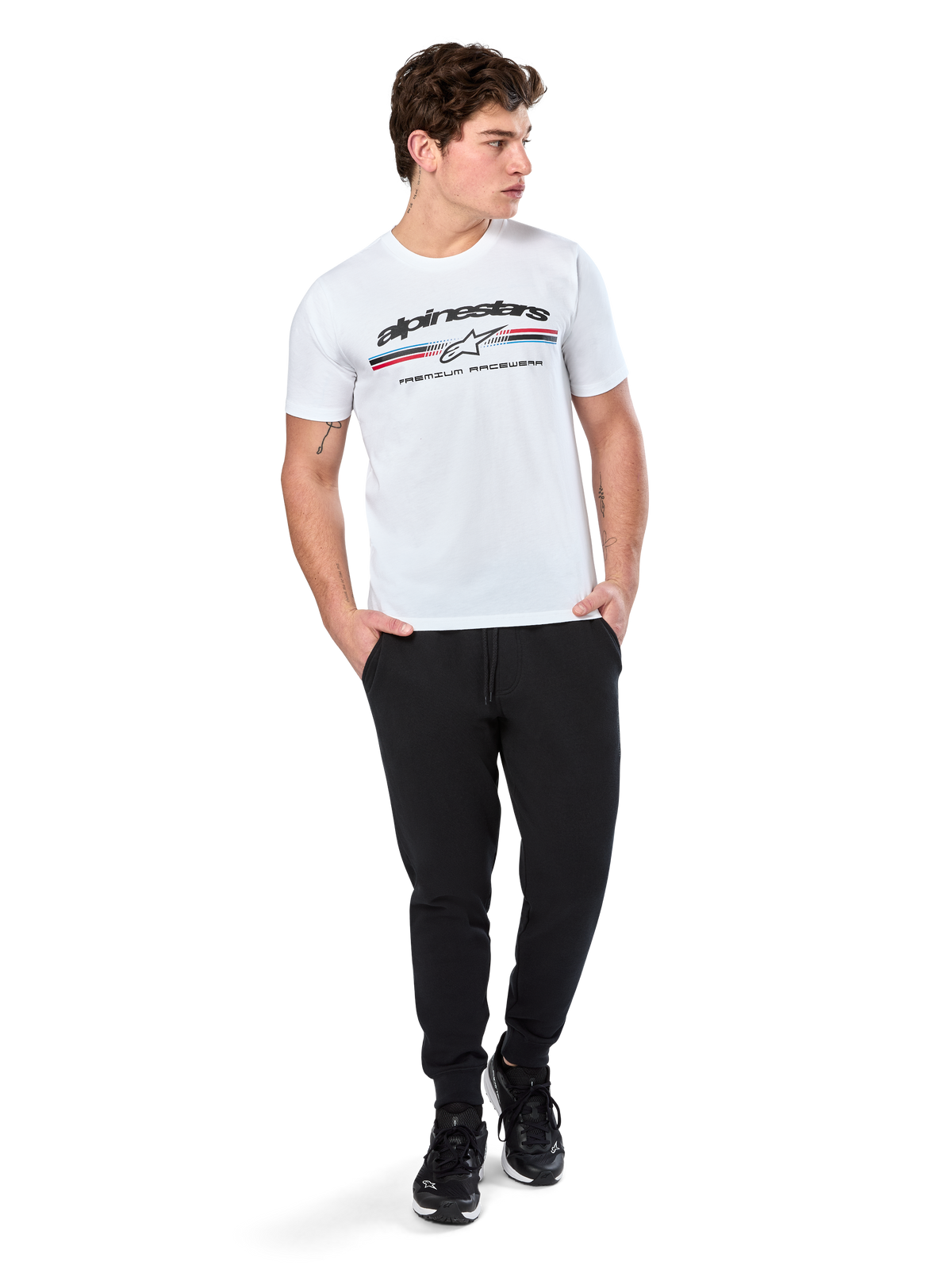 Alpinestars Prevail CSF Tee, T-shirt met korte mouwen, wit, met een driekleurig logo in paddock-stijl op de borst en Alpinestars-branding, gedragen door een model met een zwarte joggingbroek en zwarte sneakers, casual motorsport streetwear