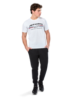 Alpinestars Prevail CSF Tee, T-shirt met korte mouwen, wit, met een driekleurig logo in paddock-stijl op de borst en Alpinestars-branding, gedragen door een model met een zwarte joggingbroek en zwarte sneakers, casual motorsport streetwear