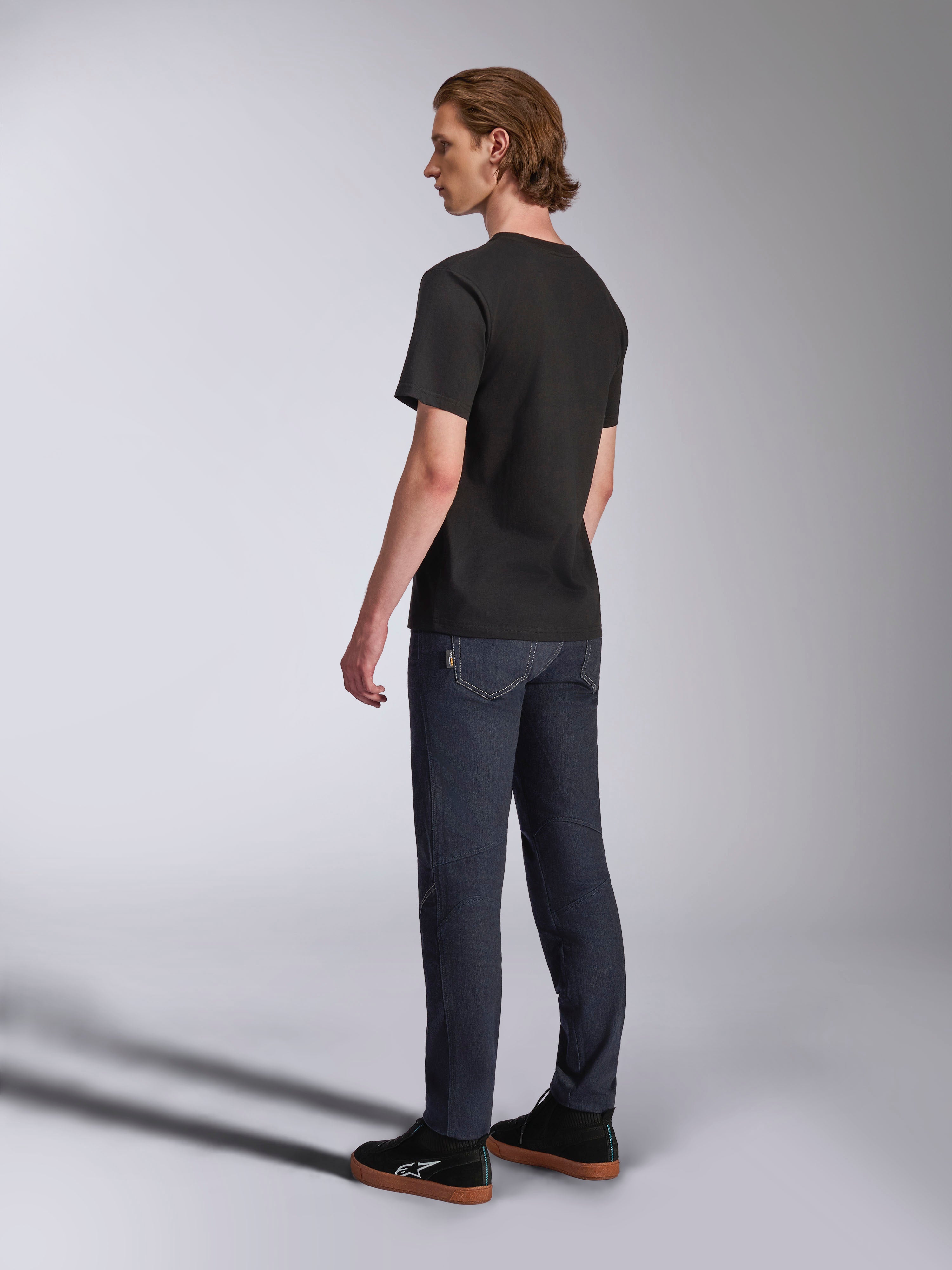 Alpinestars Luxo CSF Tee, T-shirt met korte mouwen, zwart, achteraanzicht op model in donkerblauwe jeans en zwarte sneakers, casual motorsport-geïnspireerde streetwear