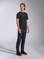 Alpinestars Luxo CSF T-shirt, T-shirt met korte mouwen, zwart, goudkleurig omlijnd Astars-logo op de borst, gedragen door model met donkere denim jeans en zwarte sneakers, casual motorsport streetwear