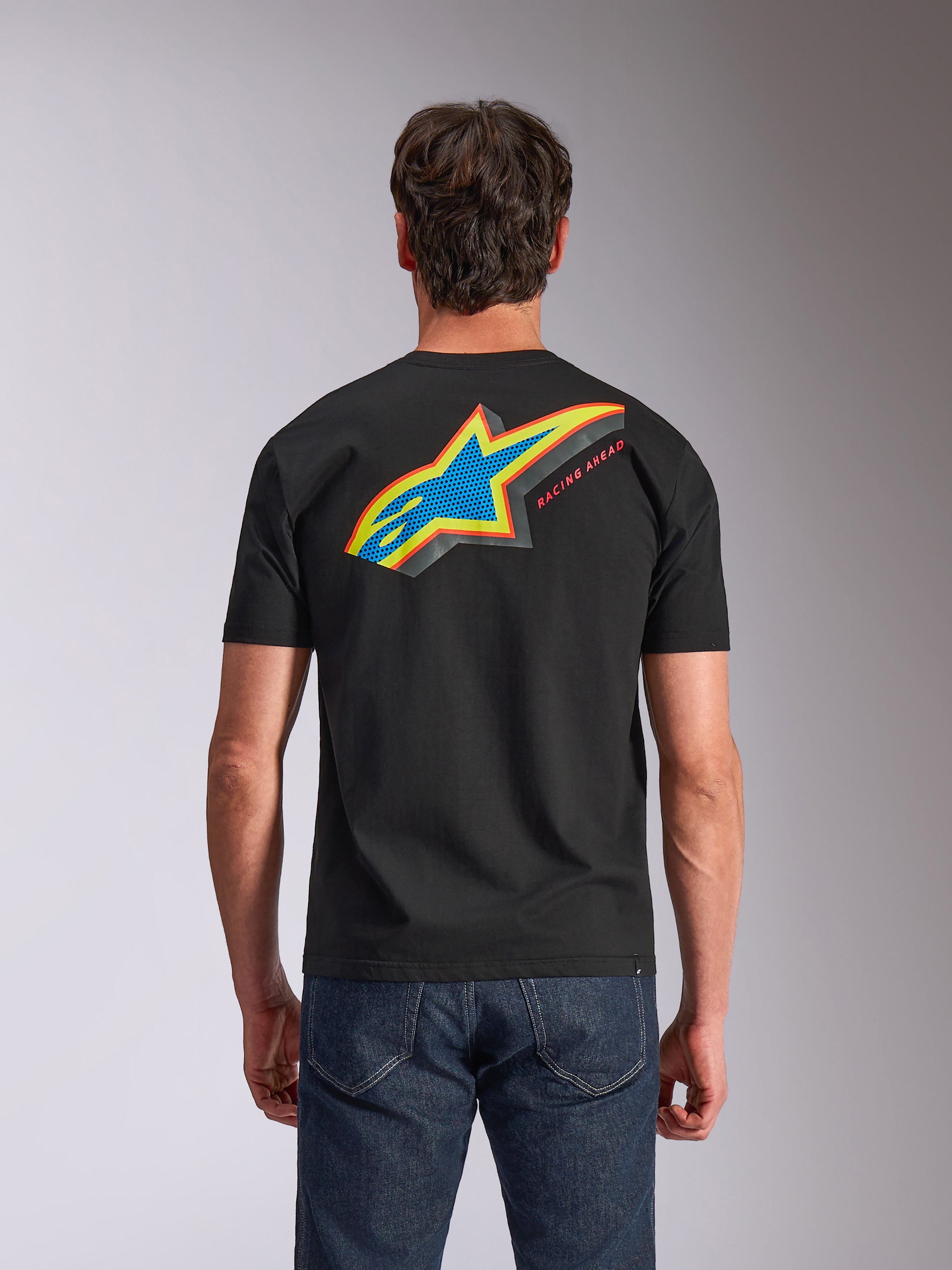 Alpinestars Angler CSF Tee, T-shirt met korte mouwen, zwart, achteraanzicht met levendig meerkleurig Astars-logo met geperforeerde print en de tekst 'RACING AHEAD', gedragen met een blauwe jeans, casual motorsport-geïnspireerde kleding