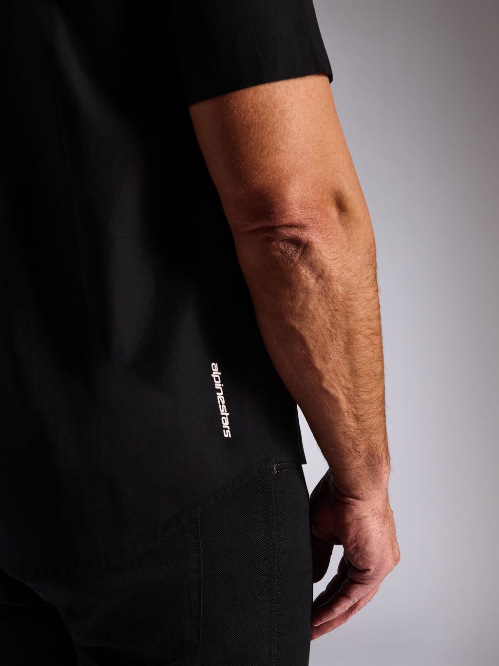Alpinestars Strive Woven Shirt, zwart overhemd met korte mouwen en knoopsluiting, verticaal wit Alpinestars-logo aan de zijkant, close-up detail van de zoom en het merklogo, casual motorsport streetwear