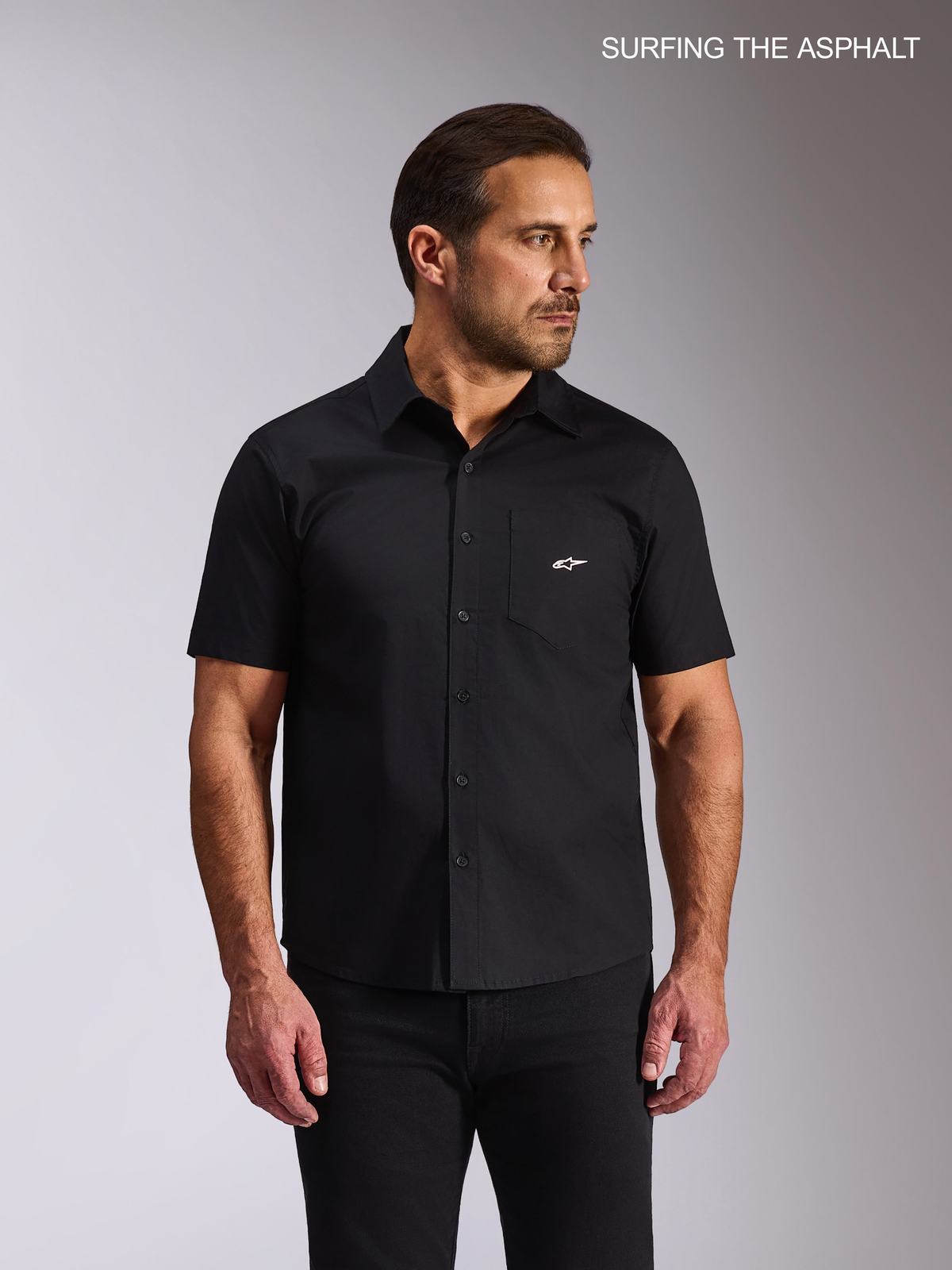Alpinestars Chemise Tissée Strive, chemise casual à manches courtes pour homme, popeline extensible noire, avec poche poitrine et logo Alpinestars blanc, portée par un modèle