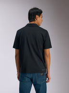 Alpinestars Impetus Sport Polo, zwart poloshirt met korte mouwen, achteraanzicht van een man die de polo draagt met een blauwe spijkerbroek, voorzien van een klein Alpinestars-woordmerk op de onderrug, casual op motorsport geïnspireerde sportkleding