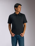 Alpinestars Impetus Sport Polo, zwarte polo met korte mouwen, sluiting met drie knopen en zelfkraag, klein grijs Astars-logo op de linkerborst, gedragen met een blauwe jeans, casual motorsport-geïnspireerde sportkleding