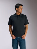 Alpinestars Impetus Sport Polo, zwarte polo met korte mouwen, sluiting met drie knopen en zelfkraag, klein grijs Astars-logo op de linkerborst, gedragen met een blauwe jeans, casual motorsport-geïnspireerde sportkleding