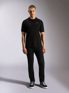 Alpinestars Endeavor Classic Polo, klassieke piqué polo met korte mouwen, zwart, klein wit Astars-logo op de borst, geribde kraag en manchetten, gedragen door model met zwarte broek en sneakers, casual motorsport streetwear