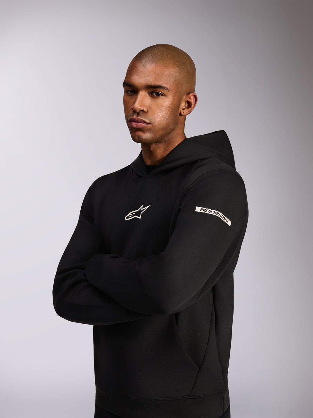 Alpinestars Insight Hoodie, casual sportswear hoodie, zwart, wit Astars-logo op de borst en woordlogo op de bovenmouw, model draagt hoodie met de armen over elkaar, premium double face fleece constructie