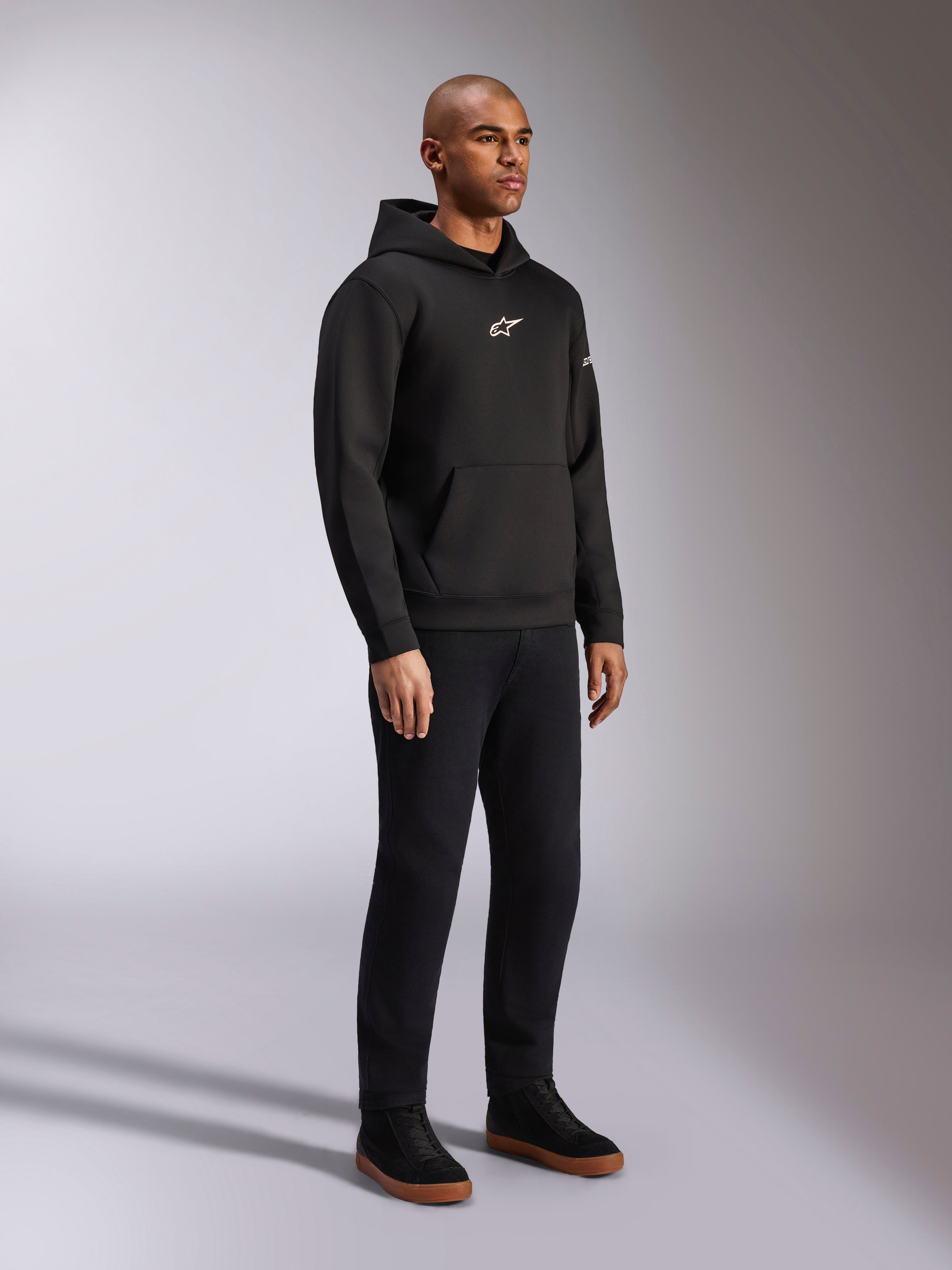 Alpinestars Insight Hoodie, zwart, casual pullover fleece hoodie met wit Astars-logo op de borst, kangoeroezak, gedragen met zwarte broek en sneakers, volledige studio-opname, motorsport-geïnspireerde streetwear