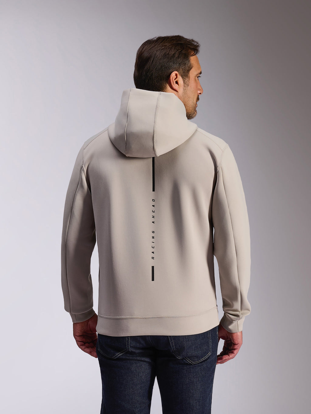 Alpinestars Insight Hoodie in Cement, achteraanzicht van model in een lichtgrijze pullover sweatshirt, voorzien van een zwart verticaal streeplogo met de tekst 'RACING AHEAD', casual op motorsport geïnspireerde hoodie van dubbelzijdige fleece.