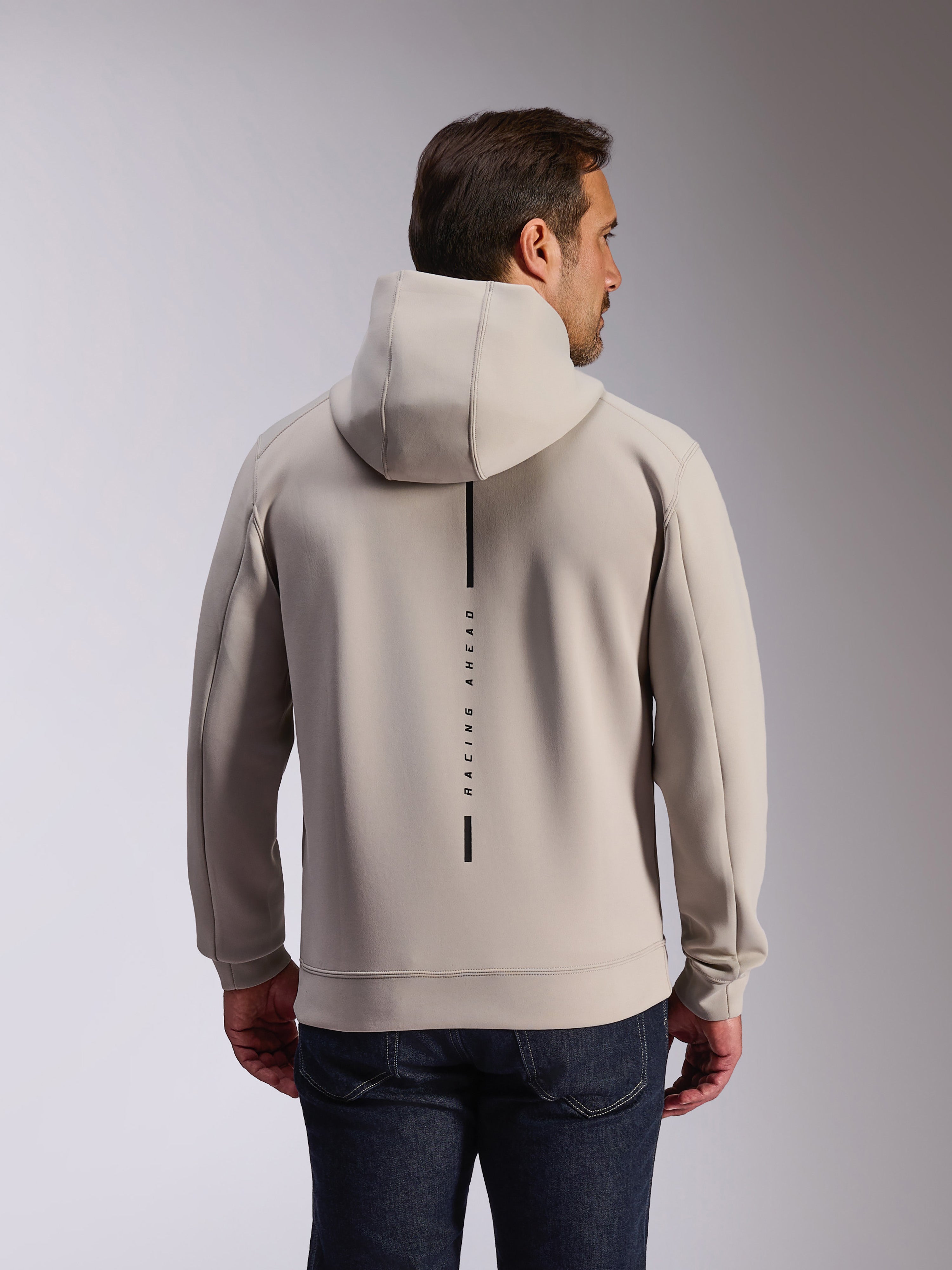 Alpinestars Insight Hoodie in Cement, achteraanzicht van model in een lichtgrijze pullover sweatshirt, voorzien van een zwart verticaal streeplogo met de tekst 'RACING AHEAD', casual op motorsport geïnspireerde hoodie van dubbelzijdige fleece.