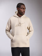 Alpinestars Emergent Oversized Hoodie, zandkleur, pullover met oversized pasvorm, ton-sur-ton 3D-geborduurd Astars-logo op de borst, kangoeroezak, capuchon met trekkoord, casual streetwear gedragen door model met zwarte broek.