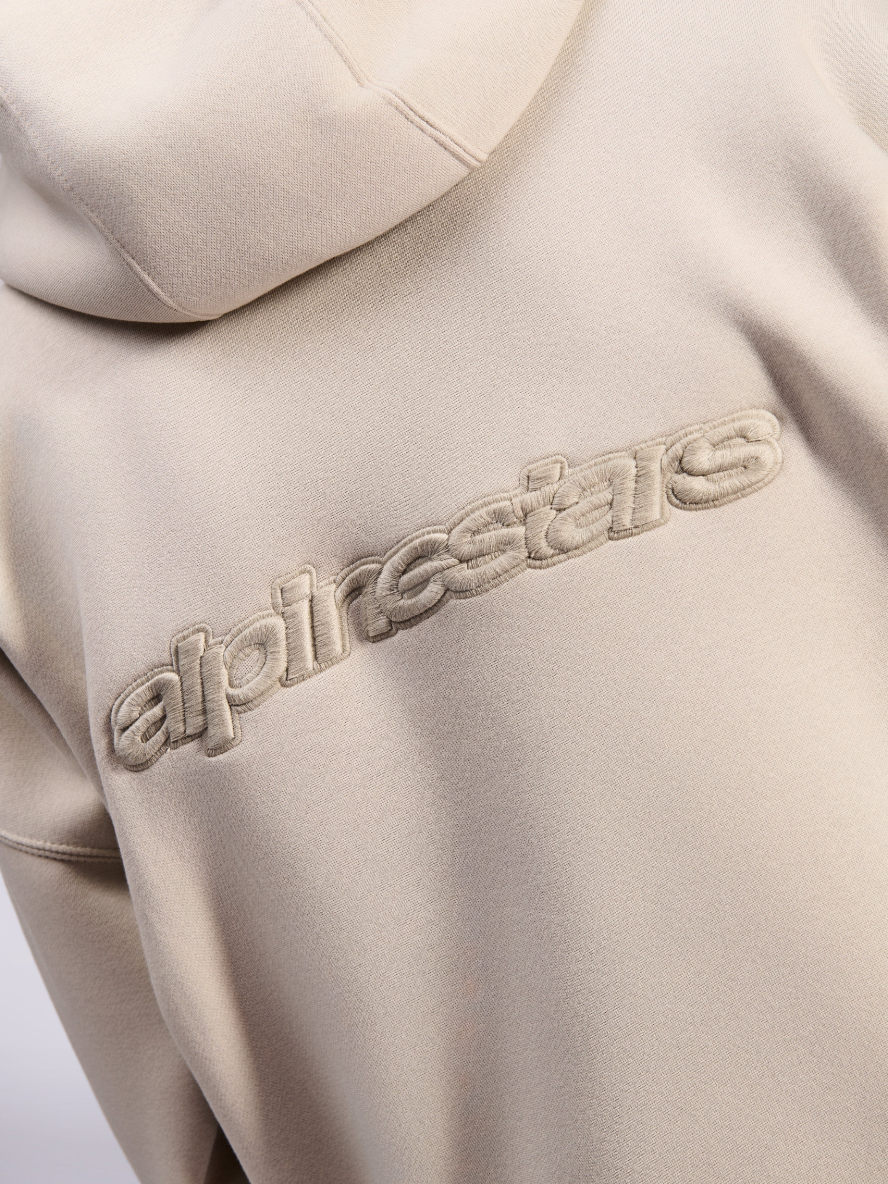 Alpinestars Emergent Oversized Hoodie, casual streetwear, zandkleur, detailweergave van tonaal 3D-geborduurd Alpinestars-woordlogo op de rug, premium fleece textuur
