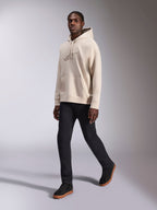 Alpinestars Emergent Oversized Hoodie, casual streetwear, zandkleurig gebroken wit, ton-sur-ton 3D geborduurd logo, gedragen door model met zwarte broek en zwarte sneakers, ontspannen oversized pasvorm met kangoeroezak en capuchon met trekkoord
