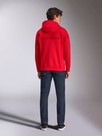 Alpinestars Emergent Oversized Hoodie, rood, achteraanzicht op mannelijk model, met toon-op-toon 3D-geborduurd Alpinestars-woordlogo, gedragen met donkerblauwe jeans, casual motorsport-geïnspireerde streetwear