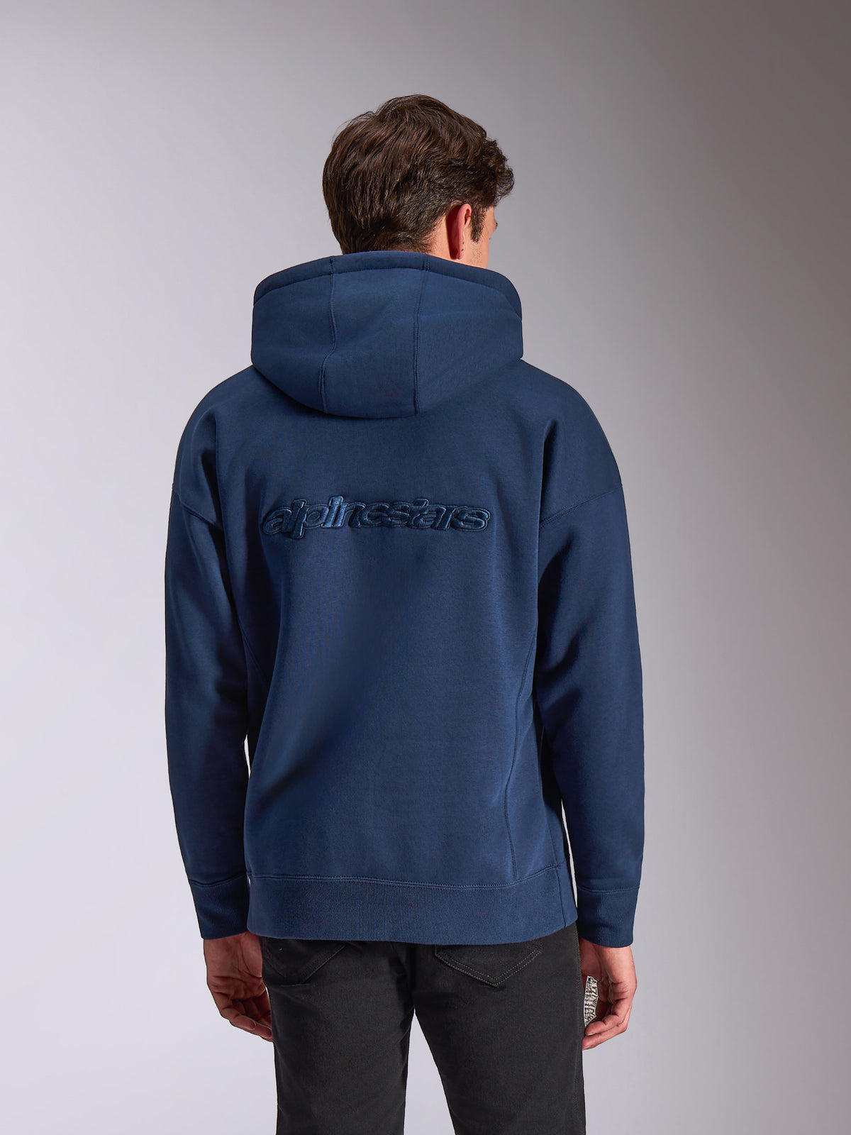 Alpinestars Emergent Oversized Hoodie, marineblauw, achteraanzicht met ton-sur-ton geborduurd Alpinestars-woordlogo, oversized pasvorm, casual fleece hoodie, capuchon met trekkoord en geribbelde manchetten, op motorsport geïnspireerde streetwear.