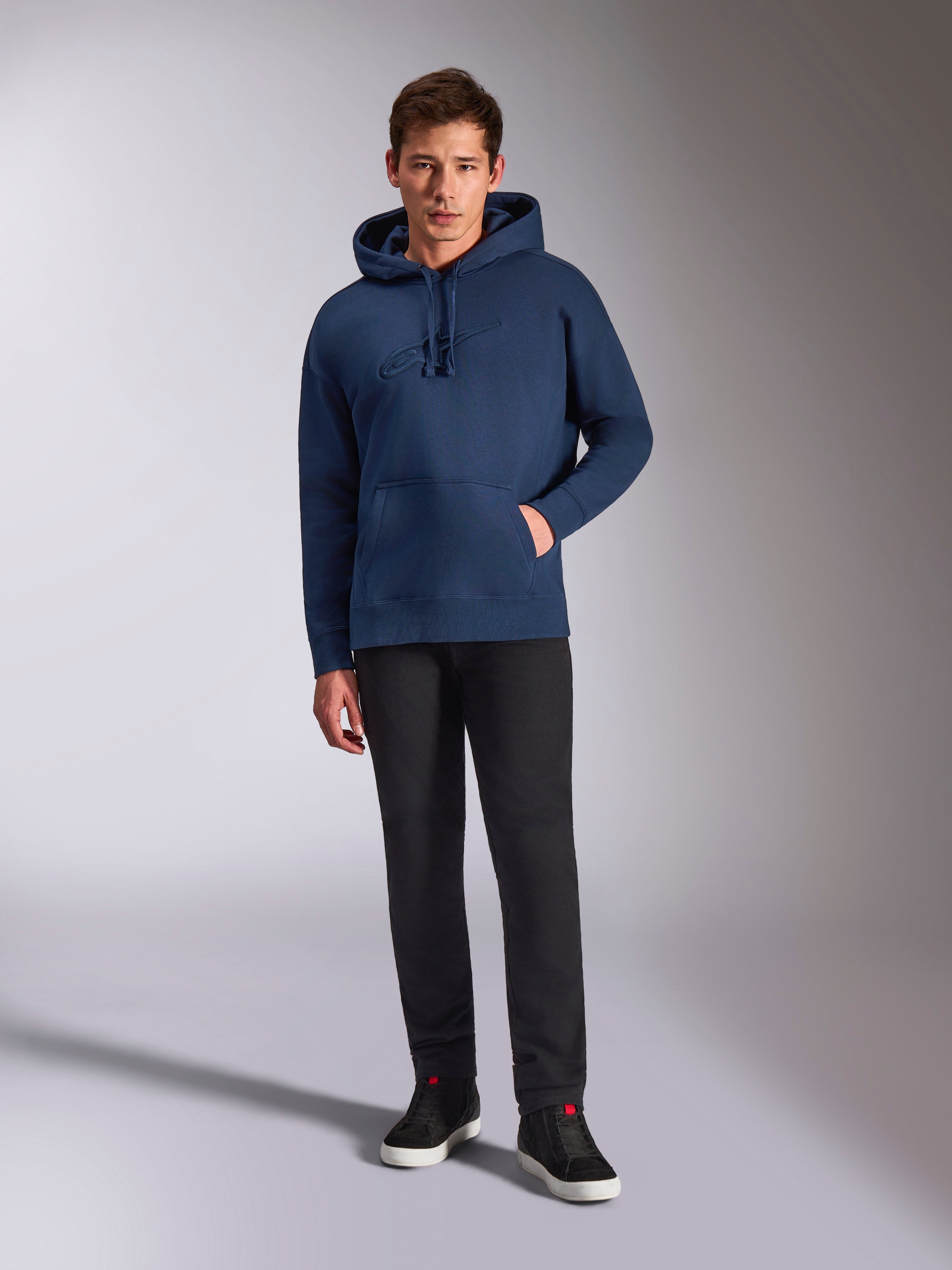 Alpinestars Emergent Oversized Hoodie, navy blauwe pullover fleece hoodie, tonaal 3D-geborduurd logo op de voorkant, gedragen door model met zwarte broek en sneakers, casual streetwear stijl.
