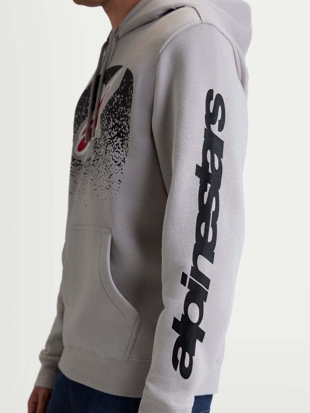 Alpinestars Obsessed Hoodie, casual motorsport-pullover van fleece, unisex, grijs en zwart, zijaanzicht op model met verticale Alpinestars-branding op de mouw en een op MX geïnspireerd verlooplogo op de borst, constructie van premium katoen en gerecycled polyester.