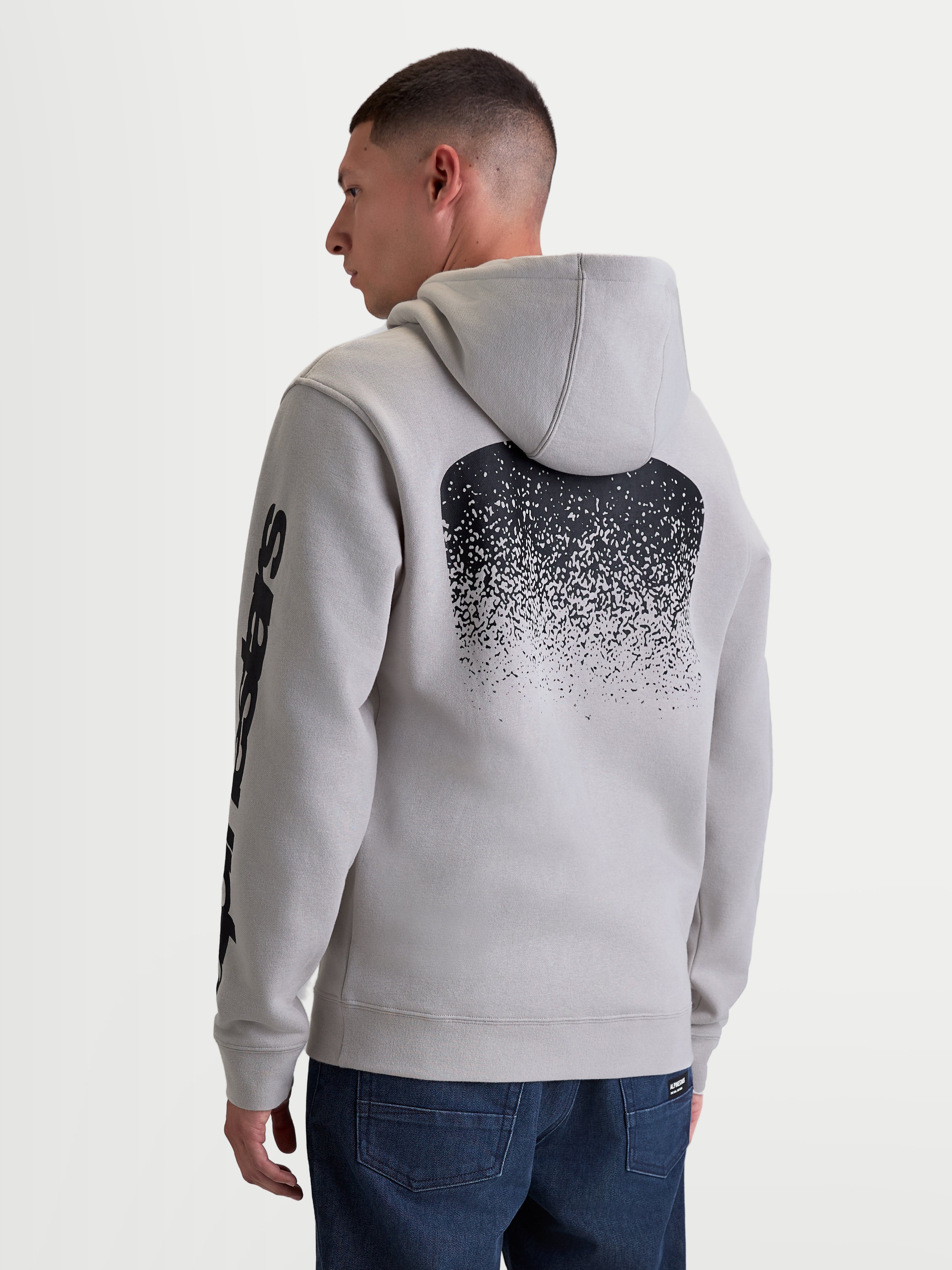 Alpinestars Obsessed hoodie, heren sportswear pullover fleece in cement grijs, voorzien van een grote zwarte MX-geïnspireerde gradiënt graphic op de rug en mouwlogo's, achteraanzicht op model, casual motorsport lifestyle kleding.