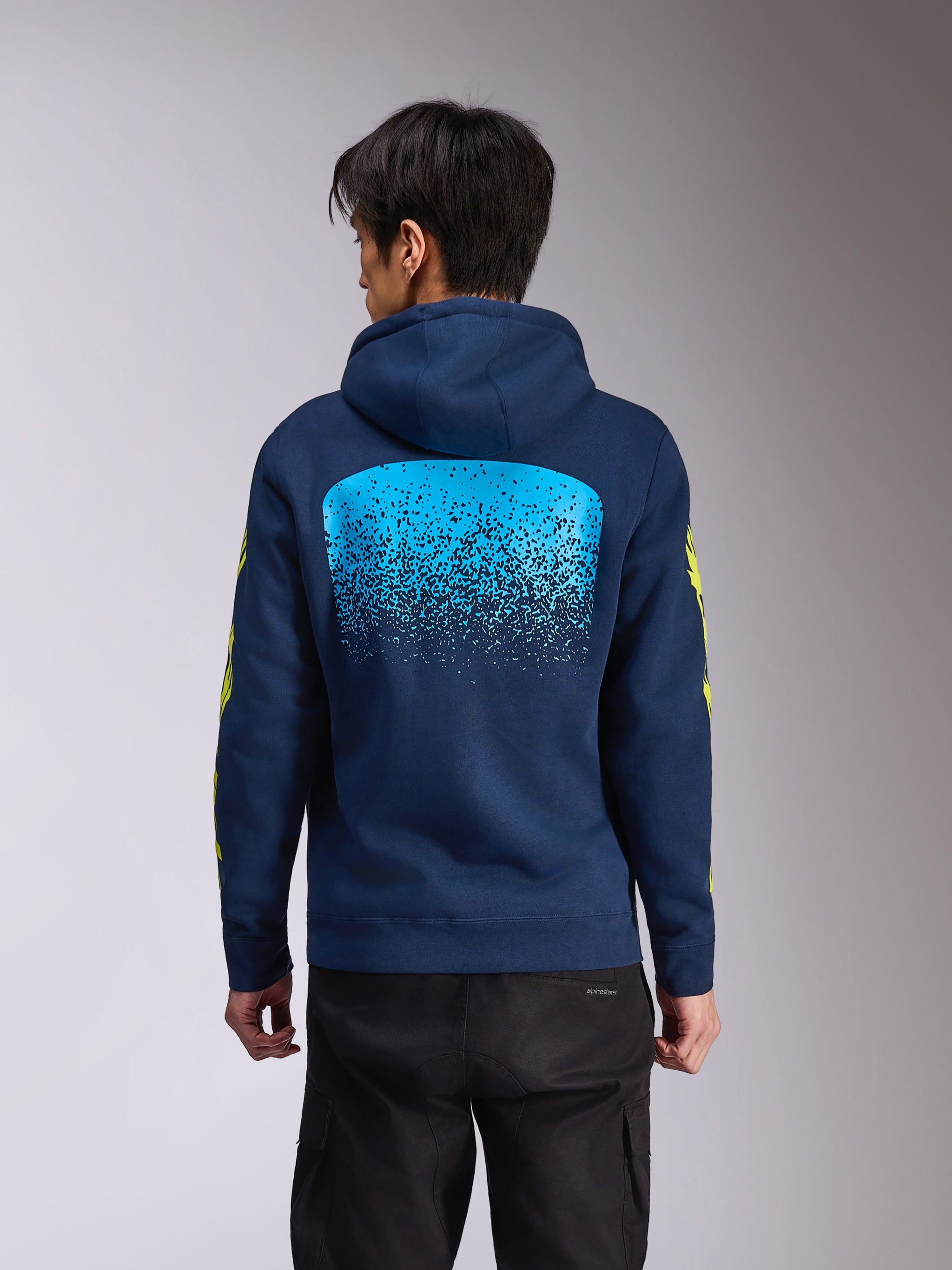 Alpinestars Obsessed Hoodie, marineblauer Kapuzenpullover aus Fleece, Rückansicht mit einer großen hellblauen MX-Farbverlaufsgrafik, gelber Alpinestars-Schriftzug auf den Ärmeln, lässige vom Motorsport inspirierte Streetwear