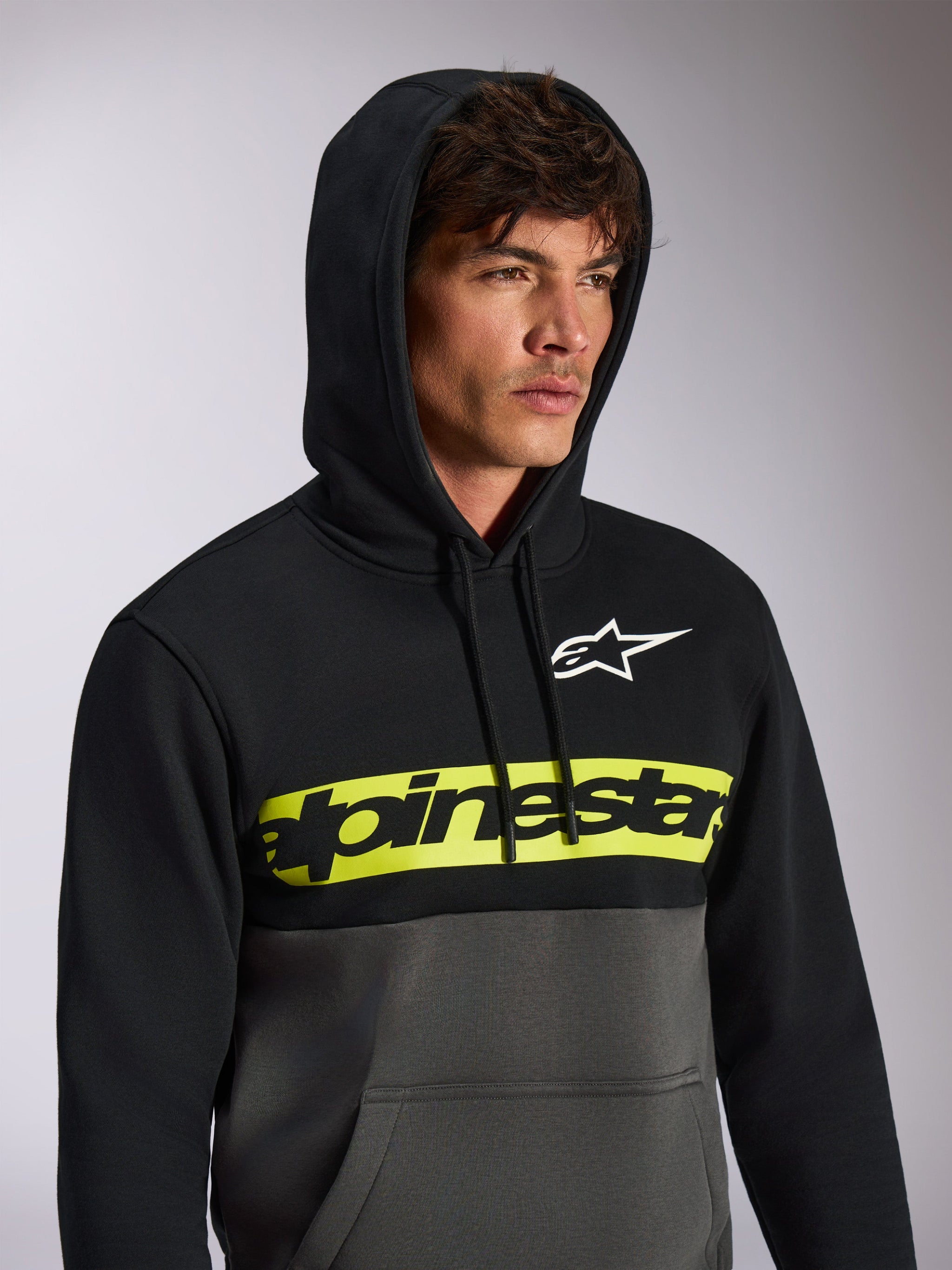 Alpinestars Parallel Hoodie, casual color-blocked streetwear, zwarte bovenkant en gunmetal grijze onderkant, neongele borstband met zwart Alpinestars-woordlogo, wit Astars-logo, hoodie met capuchon en trekkoord