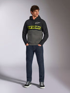 Alpinestars Parallel Hoodie, color-blocked pullover, zwart en gunmetal grijs, felgeel Alpinestars woordlogo en wit Astars-logo op de borst, gedragen door een mannelijk model met donkerblauwe jeans en zwarte sneakers, casual motorsport streetwear