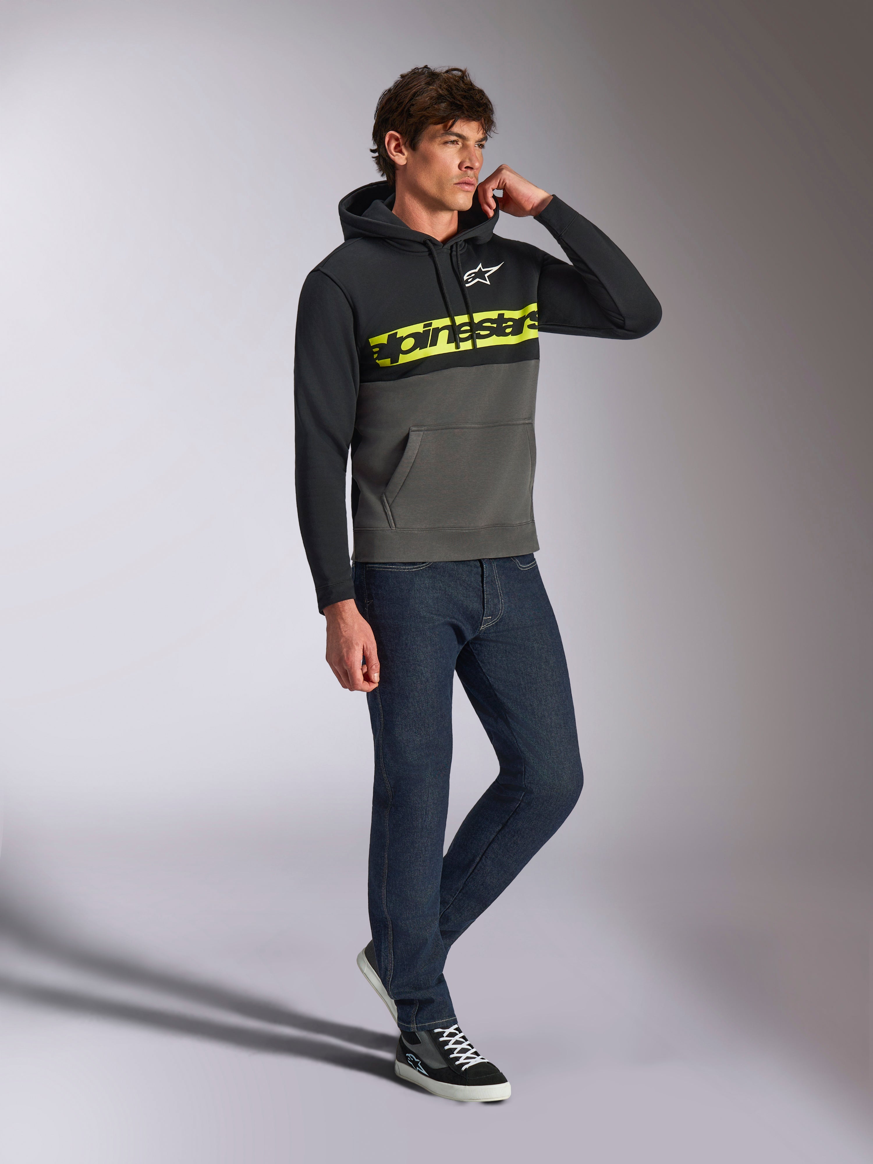 Alpinestars Parallel Hoodie, casual streetwear, kleurgeblokkeerd zwart en gunmetal grijs, neongeel Alpinestars-woordlogo op de borst, wit Astars-logo, capuchon met trekkoord, gedragen met donkere jeans en sneakers