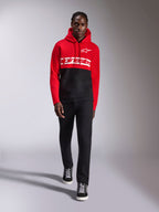 Alpinestars Parallel Hoodie, color-blocked fleece hoodie, rood en zwart, met wit Alpinestars-woordlogo op de borst en Astars-logo op de linkerborst, gedragen door een model met zwarte broek en hoge sneakers, casual motorsport streetwear