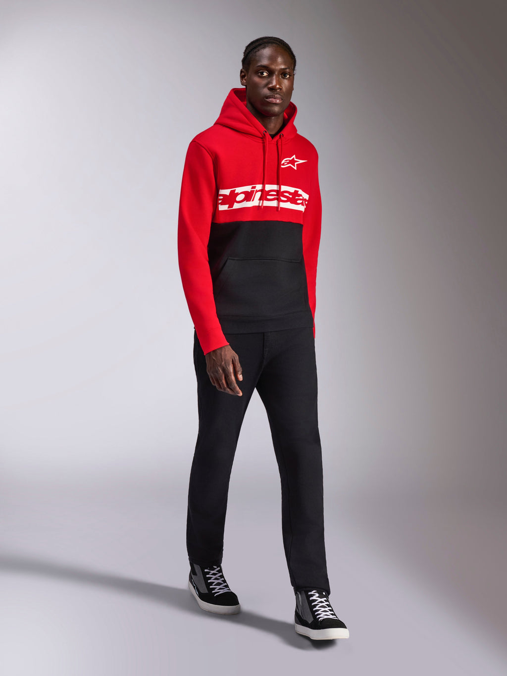 Alpinestars Parallel Hoodie, casual sportkleding, rood en zwart kleurgeblokkeerd ontwerp, met een wit Alpinestars woordmerk en sterlogo op de borst, gedragen met zwarte broek en sneakers, moderne op motorsport geïnspireerde look
