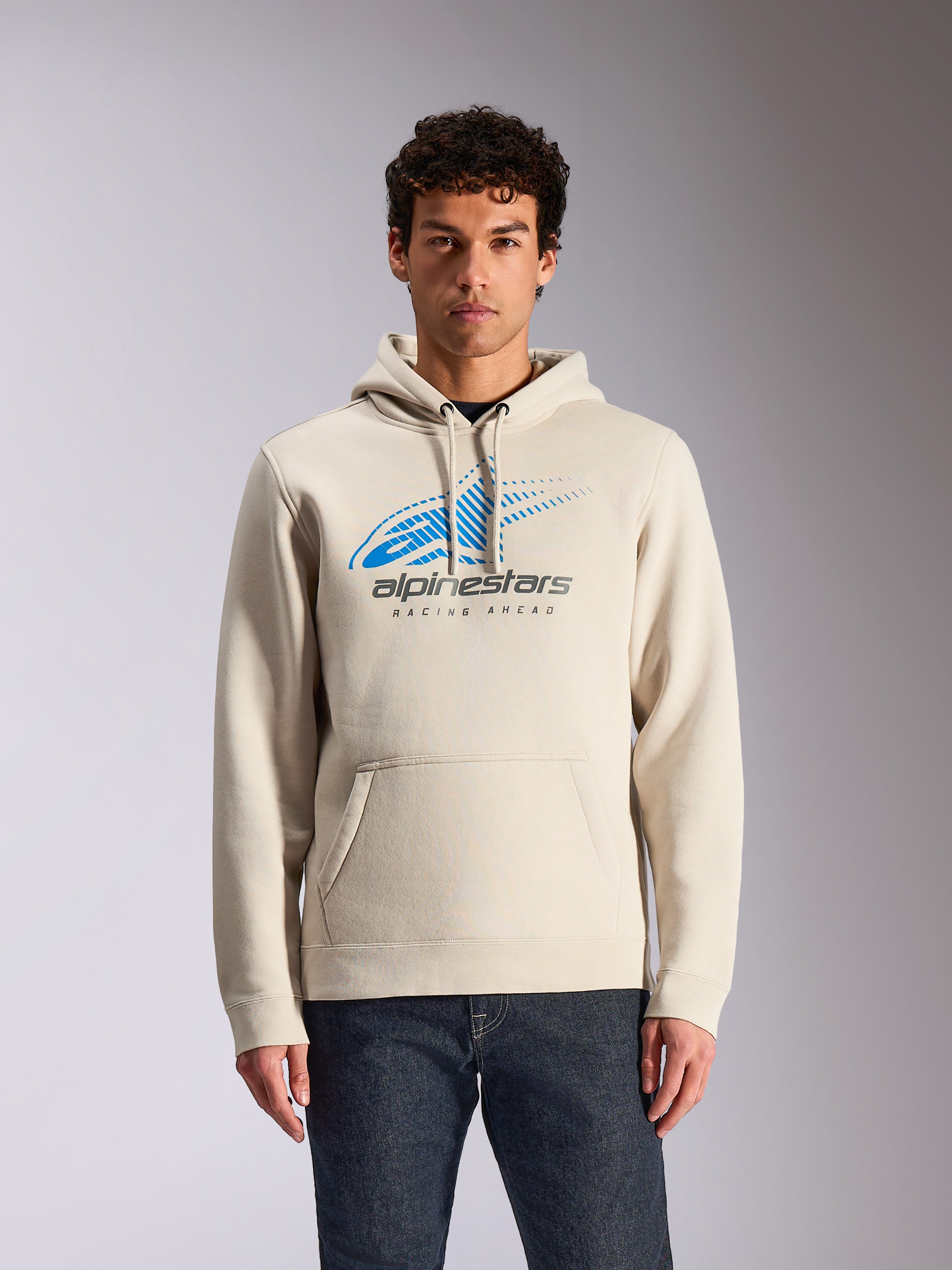 Alpinestars Pulse Hoodie, sweat à capuche décontracté blanc cassé, logo Astars Combo bleu et gris à l'avant avec motif de lignes de vitesse dégradées, poche kangourou, porté par un mannequin avec un jean foncé, streetwear inspiré du sport automobile