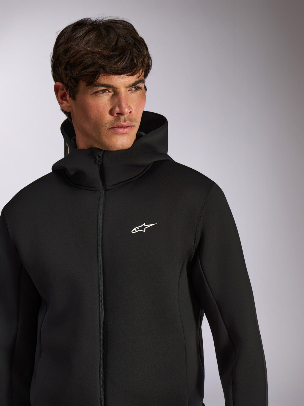 Alpinestars Cypher Hoodie, casual sportkleding, zwarte hoodie met rits en wit Astars-logo op de borst, hoge capuchon, gedragen door een mannelijk model