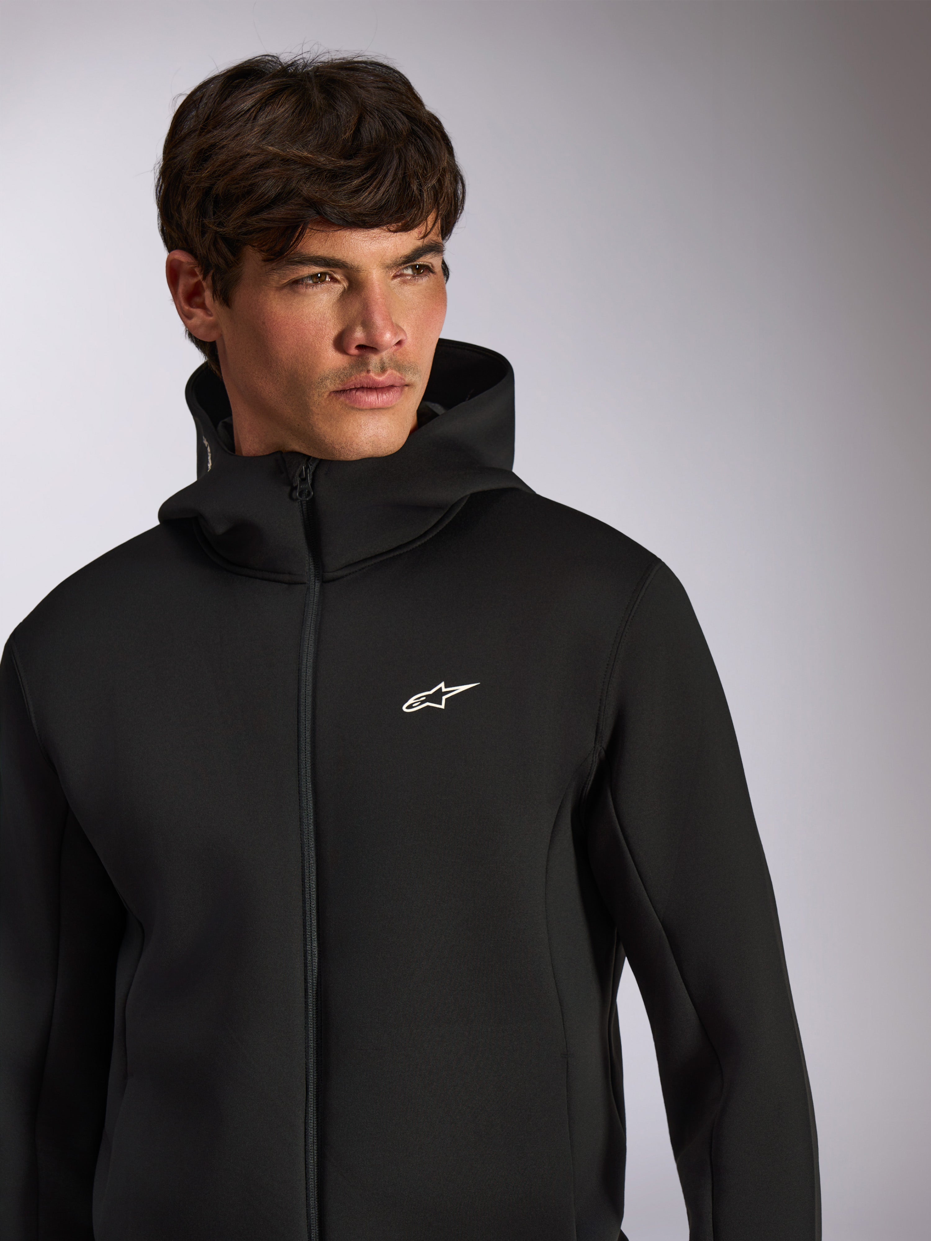Alpinestars Cypher Hoodie, casual sportkleding, zwarte hoodie met rits en wit Astars-logo op de borst, hoge capuchon, gedragen door een mannelijk model