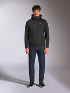 Model draagt de Alpinestars Cypher Hoodie, zwarte fleece hoodie met rits aan de voorzijde, hoge capuchon met een klein wit Astars-logo op de borst, gecombineerd met donkere denim jeans en zwarte sneakers, casual motorsport-geïnspireerde streetwear