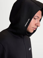 Alpinestars Cypher Kapuzenpullover, Herren-Sportswear-Kapuzenjacke mit Reißverschluss, Schwarz, Nahaufnahme am Modell mit Fokus auf die Kapuze mit hohem Kragen, weißem Alpinestars-Wortlogo und technischem Tri-Blend-Doppelvlies.