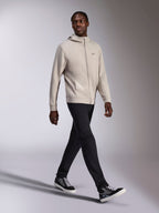Alpinestars Cypher Hoodie, Cement grijs fleecevest met rits, hoge capuchon, klein Astars-logo op de borst, gedragen door een lopend model, gecombineerd met een zwarte broek en zwart-grijze sneakers, casual motorsport-geïnspireerde sportkleding.