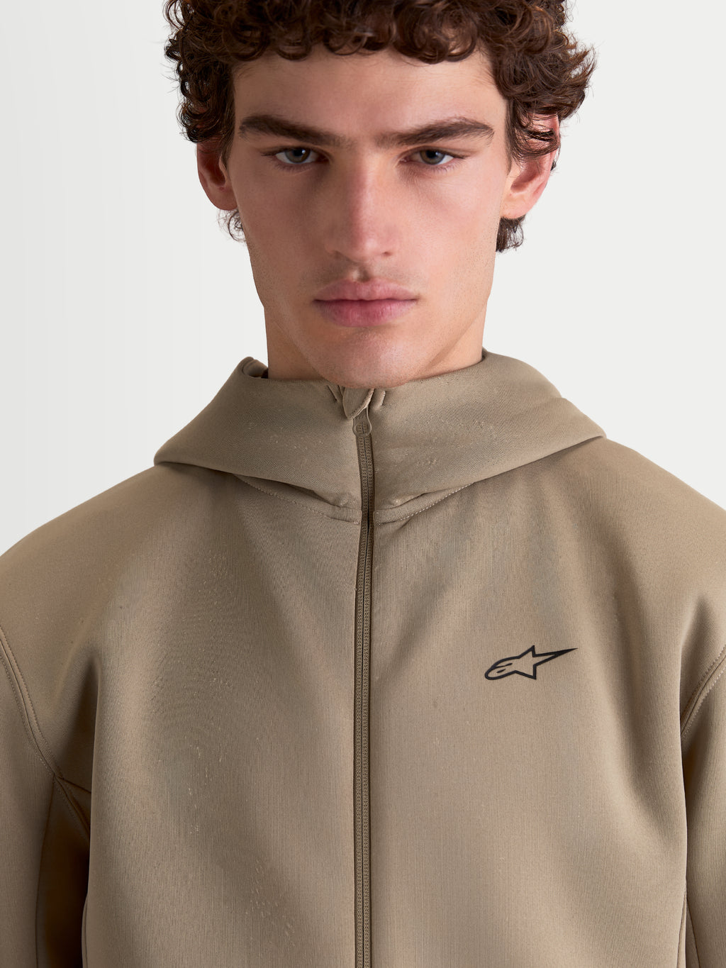 Alpinestars Cypher hoodie, beige sportswear fleece hoodie met volledige ritssluiting voor heren en dames, voorzien van een capuchon met hoge hals, technische tri-blend dubbelzijdige stof en een minimalistisch Alpinestars-logo op de borst.