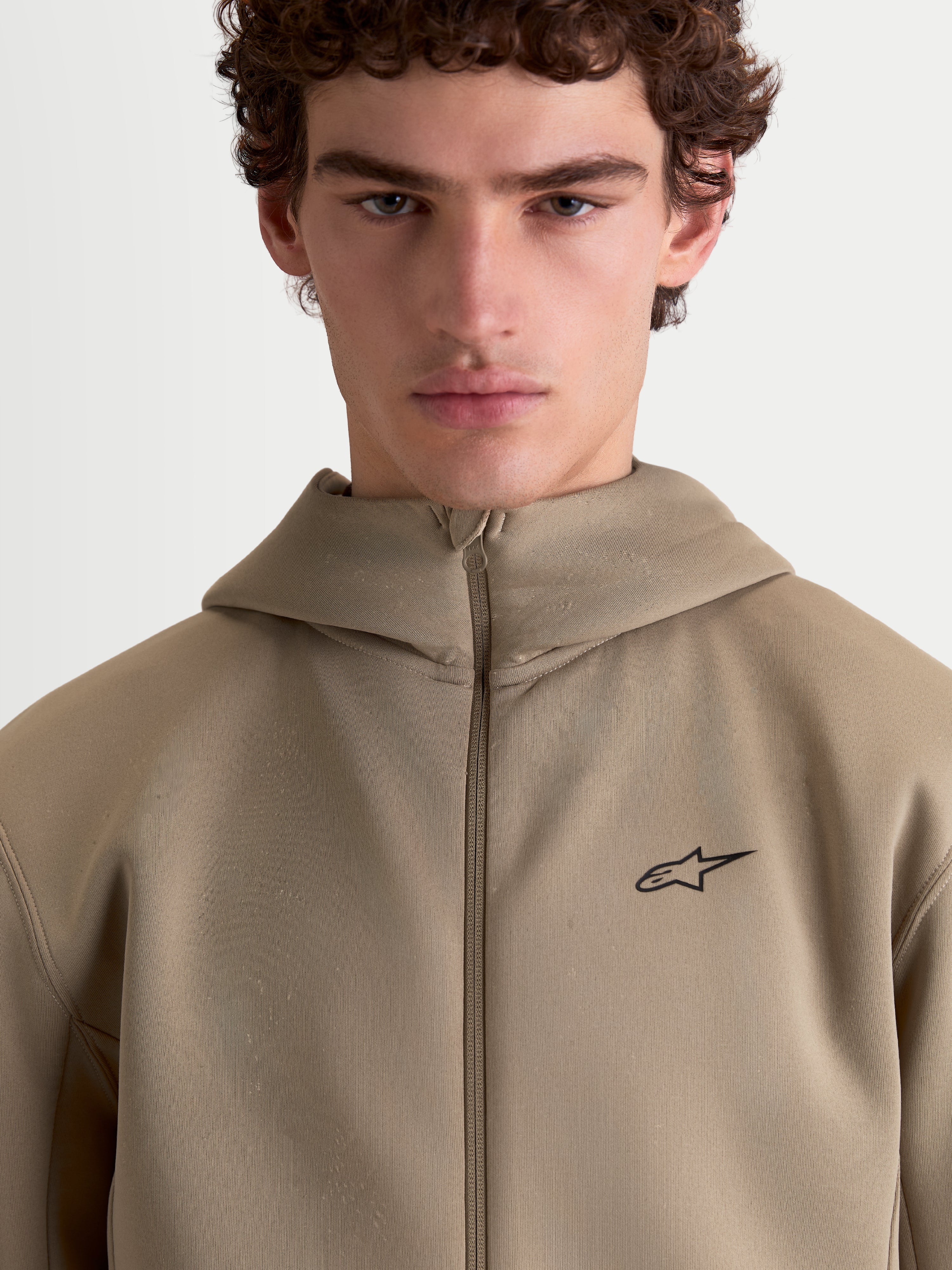 Alpinestars Cypher hoodie, beige sportswear fleece hoodie met volledige ritssluiting voor heren en dames, voorzien van een capuchon met hoge hals, technische tri-blend dubbelzijdige stof en een minimalistisch Alpinestars-logo op de borst.