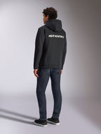 Alpinestars Transverse Hoodie, zwarte fleece hoodie met rits, achteraanzicht met een wit Alpinestars-woordlogo over de schouders, gedragen met donkerblauwe jeans en zwarte sneakers, casual op motorsport geïnspireerde streetwear