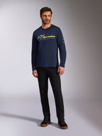 Alpinestars Mandatory CSF Tee, T-shirt met lange mouwen, donkerblauw, wit Astars-logo met neongeel woordlogo, gedragen door een model met een zwarte broek en zwarte sneakers, casual motorsport streetwear