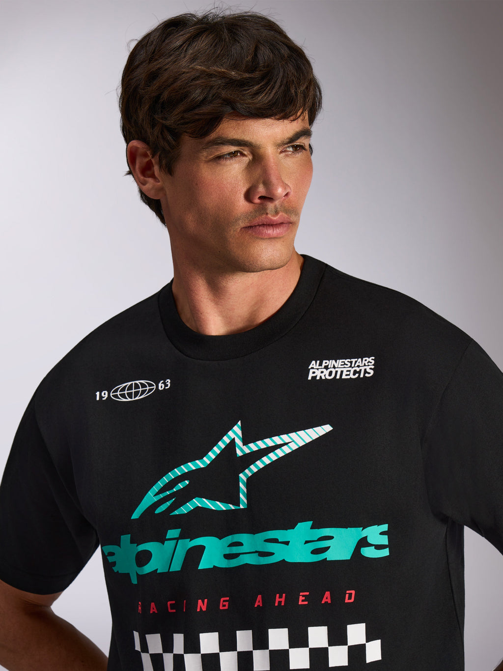 Alpinestars Aplomb Oversized CSF Tee, T-shirt met korte mouwen, zwart, teal en wit Astars combo-logo met 'Racing Ahead' tekst en geblokt patroon, gedragen door een mannelijk model, casual motorsport streetwear
