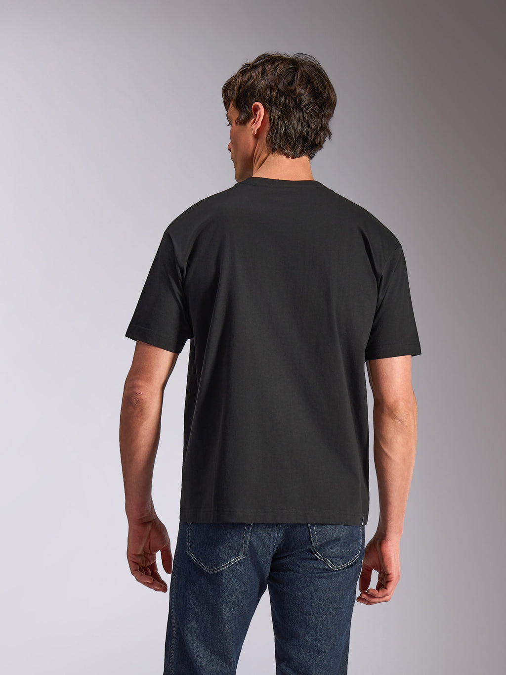 Alpinestars Aplomb Oversized CSF Tee, T-shirt met korte mouwen, zwart, achteraanzicht, gedragen door model met blauwe jeans, relaxed fit casual sportkleding