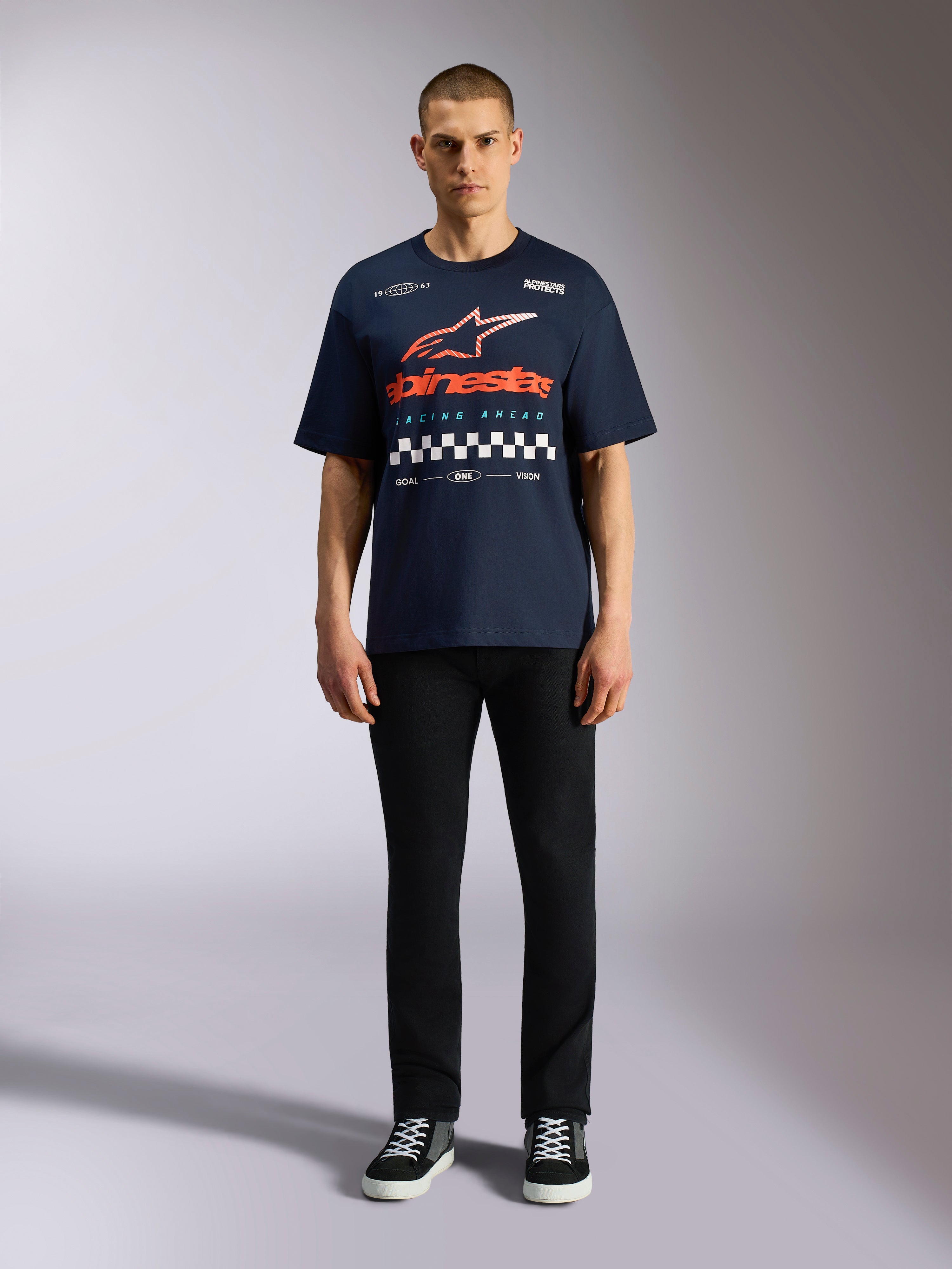 Alpinestars Aplomb Oversized CSF Tee, marineblauw T-shirt met korte mouwen, grote grafische print op de borst met oranje en rood kleurverloop logo en geblokt patroon, gedragen door model met zwarte broek en sneakers, casual motorsport streetwear