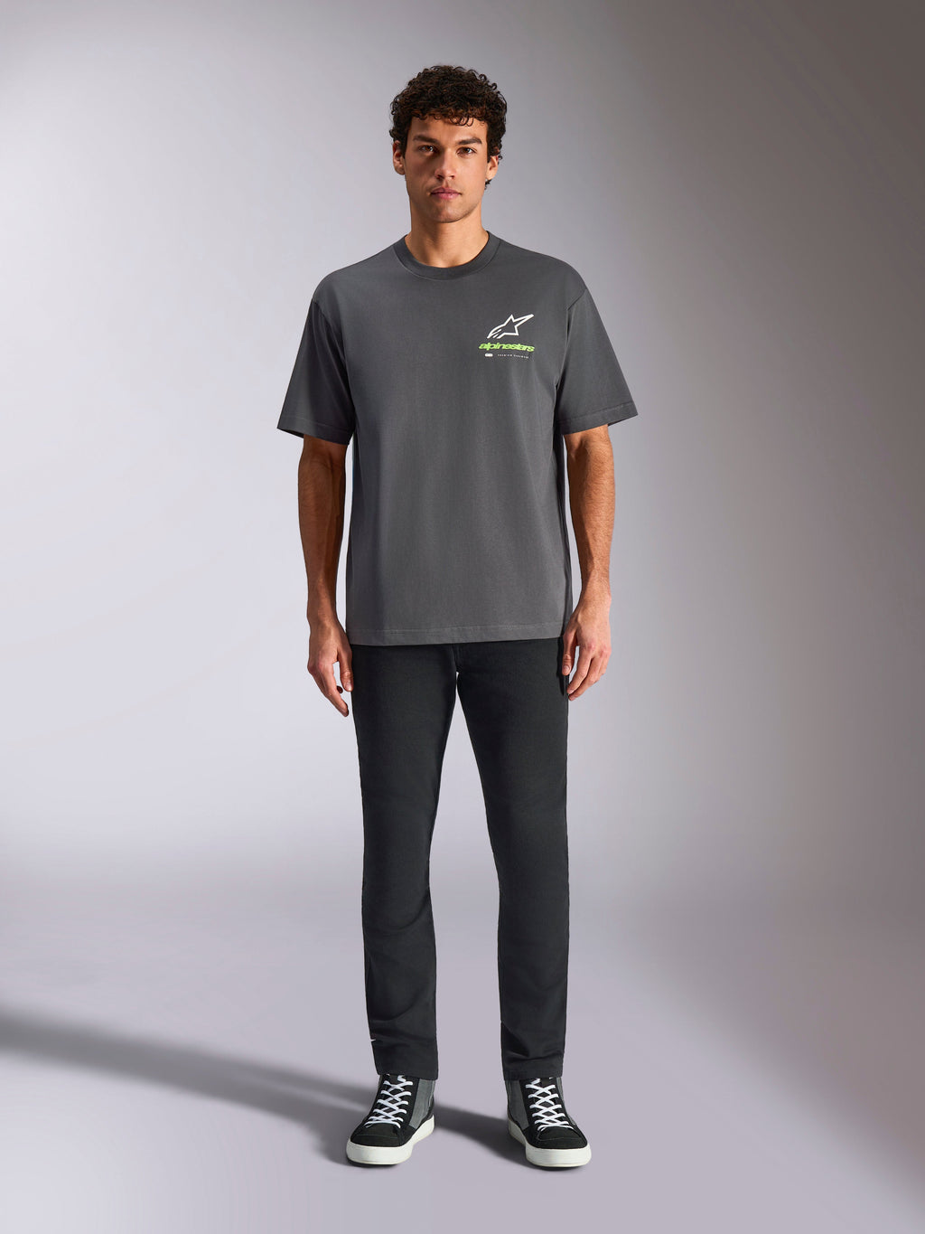 Alpinestars Overhang Oversized CSF Tee, T-shirt met korte mouwen, antracietgrijs, met een wit en limegroen Alpinestars-logo op de voorkant, gedragen door een model met een zwarte broek en sneakers, relaxte casual streetwear