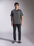 Alpinestars Overhang Oversized CSF Tee, T-shirt met korte mouwen, antracietgrijs, met een wit en limegroen Alpinestars-logo op de voorkant, gedragen door een model met een zwarte broek en sneakers, relaxte casual streetwear