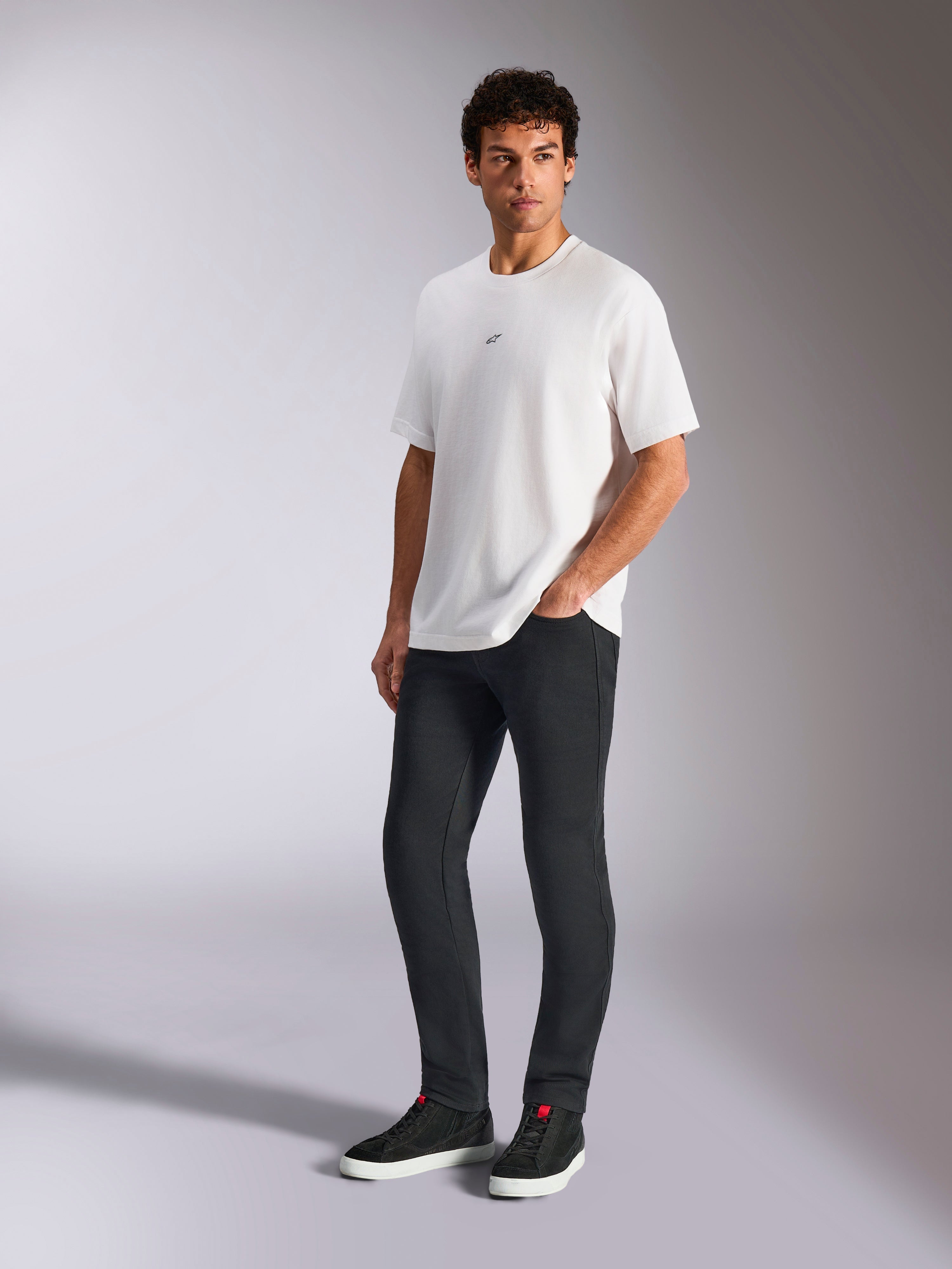 Alpinestars Focused Oversized CSF Tee, T-shirt met korte mouwen, wit, met een klein zwart Astars-logo op de borst, gedragen door een mannelijk model met een donkere broek en zwarte sneakers, casual motorsport-geïnspireerde streetwear