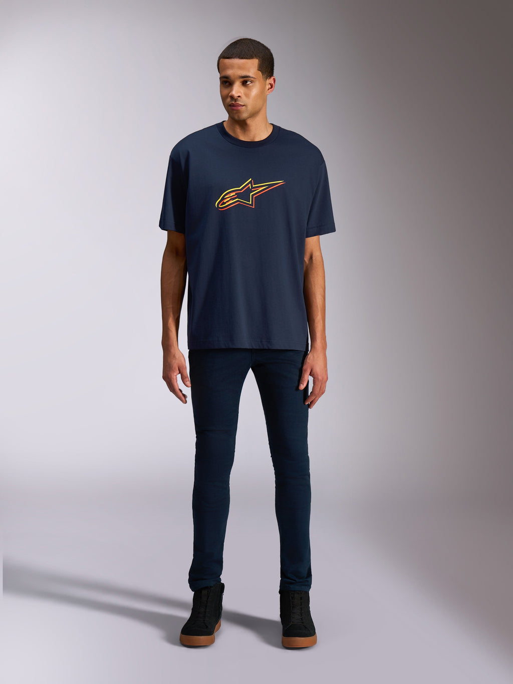 Alpinestars Alter Oversized CSF Tee, T-shirt met korte mouwen, donkerblauw, voorzien van een Alpinestars-stervormig logo op de voorkant met een geel en oranje kleur-offset, gedragen door een model met donkere denim en zwarte sneakers, casual lifestyle sportkleding.